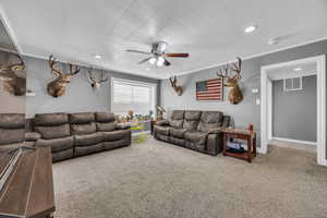 Carpeted living room with ceiling fan and ornamental molding