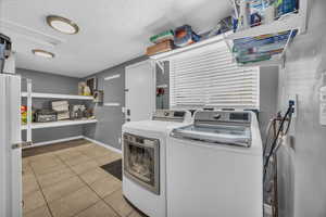 Washroom featuring a textured ceiling, light tile patterned flooring, and washing machine and clothes dryer