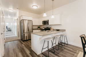 Kitchen with pendant lighting, white cabinetry, appliances with stainless steel finishes, and kitchen peninsula