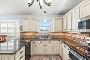 Kitchen featuring cream cabinetry, appliances with stainless steel finishes, dark stone counters, hanging light fixtures, and sink