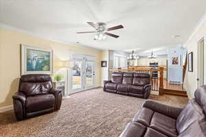 Living room with carpet floors, a textured ceiling, crown molding, and ceiling fan with notable chandelier