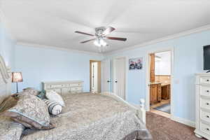 Carpeted bedroom with ceiling fan, ensuite bath, and crown molding