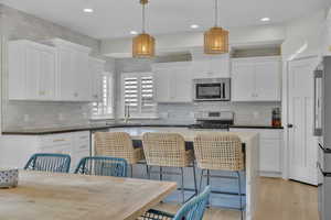 Kitchen with hanging light fixtures, white cabinets, and appliances with stainless steel finishes