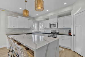 Kitchen with white cabinetry, stainless steel appliances, decorative light fixtures, dark stone counters, and a kitchen island