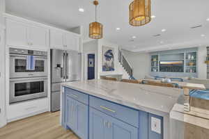 Kitchen with decorative light fixtures, a kitchen island, light wood-type flooring, appliances with stainless steel finishes, and blue cabinets