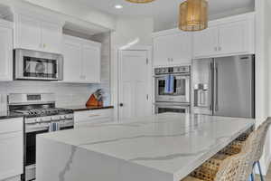 Kitchen featuring decorative light fixtures, white cabinets, light stone countertops, and stainless steel appliances