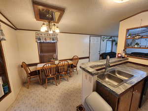 Kitchen featuring kitchen peninsula, dark brown cabinets, a textured ceiling, crown molding, and sink