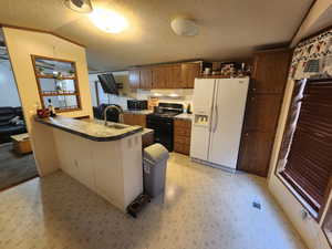 Kitchen featuring kitchen peninsula, vaulted ceiling, a textured ceiling, black appliances, and sink