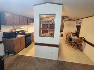 Kitchen with a textured ceiling, crown molding, light colored carpet, and black appliances