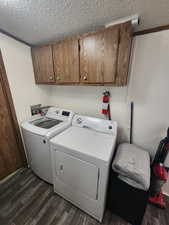 Laundry room featuring washer and clothes dryer, dark hardwood / wood-style floors, a textured ceiling, cabinets, and ornamental molding