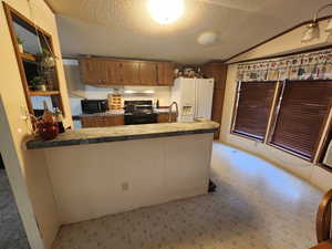 Kitchen featuring white refrigerator with ice dispenser, range, kitchen peninsula, and vaulted ceiling