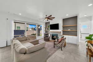 Living room with ceiling fan, built in shelves, and a tiled fireplace