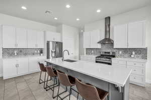 Kitchen featuring a breakfast bar, sink, appliances with stainless steel finishes, an island with sink, and wall chimney exhaust hood