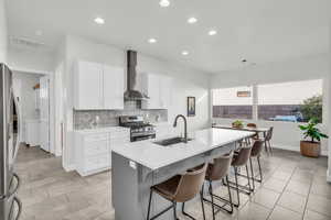 Kitchen featuring wall chimney range hood, a breakfast bar, sink, an island with sink, and stainless steel appliances