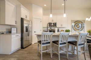 Kitchen featuring pendant lighting, light stone counters, stainless steel appliances, and white cabinetry