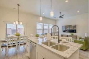 Kitchen with an island with sink, light stone countertops, pendant lighting, stainless steel dishwasher, and sink