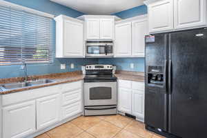 Kitchen with appliances with stainless steel finishes, sink, white cabinetry, and light tile patterned flooring