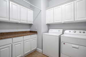 Clothes washing area with cabinets, light tile patterned flooring, and washing machine and clothes dryer