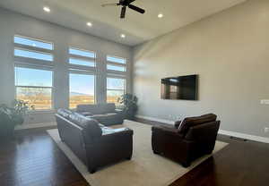 Living room with ceiling fan, dark hardwood / wood-style flooring, and a high ceiling