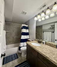 Full bathroom with a textured ceiling, tile patterned floors, vanity, toilet, and shower / bath combo with shower curtain