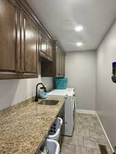 Washroom with light tile patterned floors, cabinets, washer and dryer, and sink