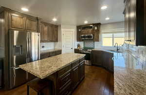 Kitchen with a center island, sink, dark brown cabinetry, dark wood-type flooring, and appliances with stainless steel finishes