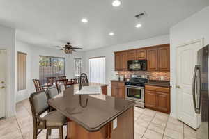 Kitchen featuring light tile patterned floors, backsplash, appliances with stainless steel finishes, and a center island with sink