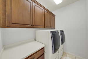 Laundry room featuring cabinets, light tile patterned floors, and independent washer and dryer