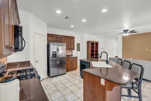 Kitchen featuring light tile patterned floors, a kitchen bar, a center island with sink, black appliances, and sink