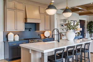 Kitchen featuring custom exhaust hood, beam ceiling, an island with sink, and tasteful backsplash