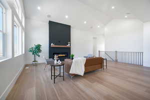 Living room featuring high vaulted ceiling, a large fireplace, and light wood-type flooring