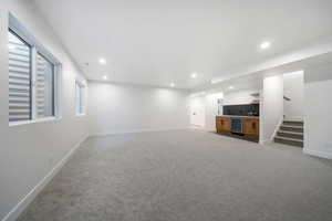 Unfurnished living room with light carpet, a healthy amount of sunlight, wine cooler, and bar