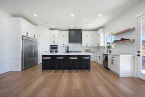 Kitchen featuring a center island, wall chimney exhaust hood, a kitchen bar, stainless steel appliances, and light wood-type flooring