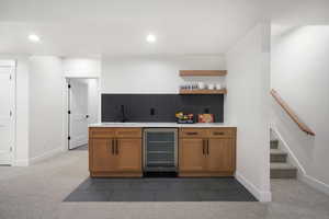 Kitchen featuring wine cooler, sink, tasteful backsplash, and dark colored carpet