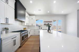 Kitchen featuring light hardwood / wood-style flooring, light stone countertops, range with two ovens, white cabinets, and wall chimney exhaust hood