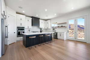 Kitchen with appliances with stainless steel finishes, white cabinets, wall chimney exhaust hood, light hardwood / wood-style flooring, and a center island