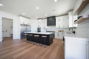 Kitchen featuring light hardwood / wood-style flooring, premium appliances, wall chimney range hood, white cabinets, and a center island