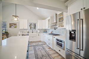 Kitchen with white cabinets, appliances with stainless steel finishes, wall chimney exhaust hood, decorative backsplash, and hanging light fixtures