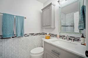 Bathroom with toilet, vanity, and tile walls