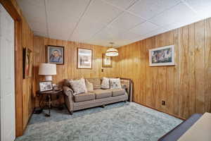 Living room with a paneled ceiling, carpet flooring, and wood walls