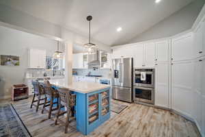 Kitchen featuring a kitchen bar, white cabinets, appliances with stainless steel finishes, and lofted ceiling