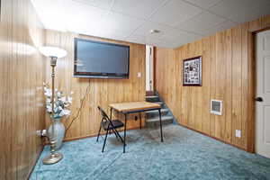 Office area featuring carpet flooring, heating unit, a drop ceiling, and wooden walls