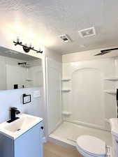 Bathroom featuring a textured ceiling, vanity, toilet, walk in shower, and hardwood / wood-style flooring