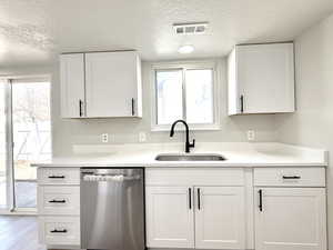 Kitchen with white cabinets, dishwasher, sink, and a textured ceiling