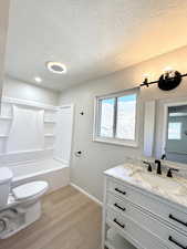 Full bathroom with toilet, hardwood / wood-style flooring, shower / washtub combination, a textured ceiling, and vanity