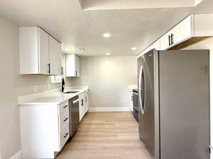 Kitchen featuring sink, light wood-type flooring, stainless steel appliances, a textured ceiling, and white cabinets