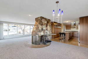 Interior space with carpet, wall chimney exhaust hood, a notable chandelier, and a textured ceiling