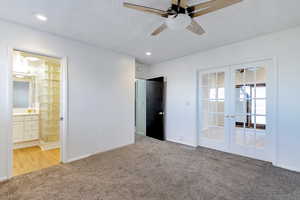 Primary bedroom featuring a textured ceiling, connected bathroom, french doors, carpet flooring, and ceiling fan