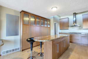 Kitchen featuring stainless steel gas stovetop, a breakfast bar area, light wood-type flooring, wall chimney exhaust hood, and a center island