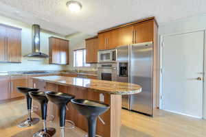 Kitchen featuring a textured ceiling, stainless steel appliances, wall chimney exhaust hood, and a kitchen island